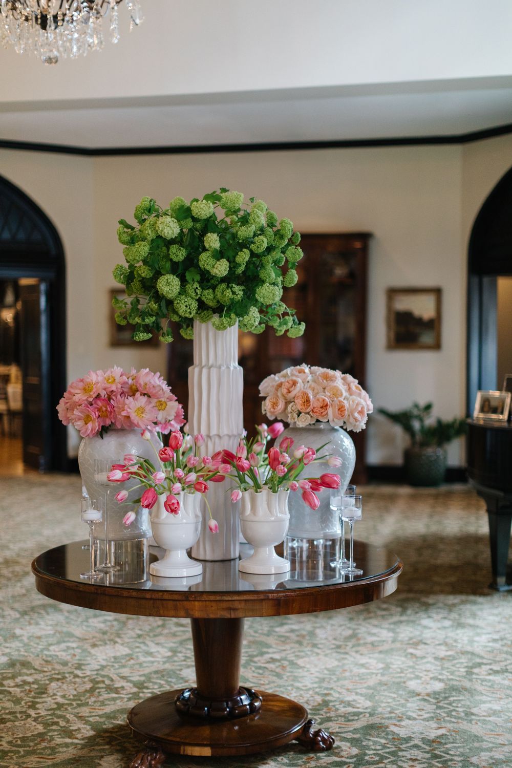 Elegant floral centerpiece arrangement with green, pink and peach blooms in white vases on a round wooden table.