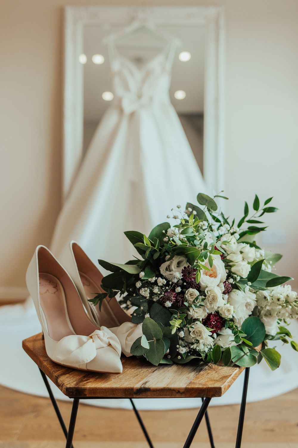 Bridal accessories including white heels and floral bouquet arranged on wooden chair.