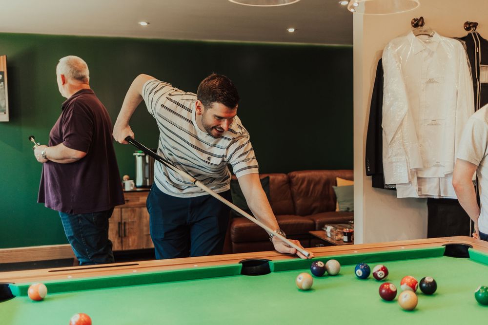 People playing pool at a casual gathering around a green billiards table.
