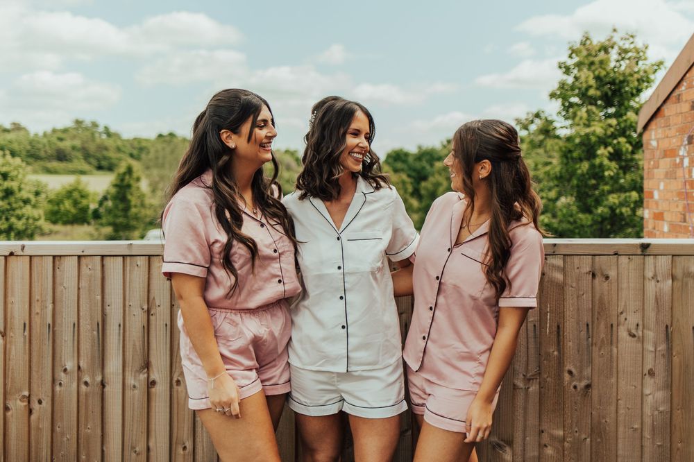 Women in matching pink shirts sitting outdoors on a sunny day with a wooden fence in the background.