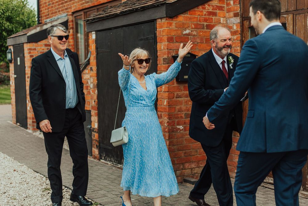 Wedding guests in formal attire greet each other outside a brick building entrance.