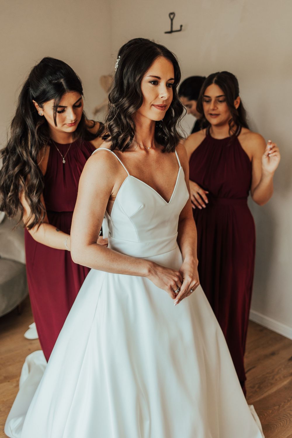Bridesmaids in burgundy dresses help the bride with her elegant white wedding gown.