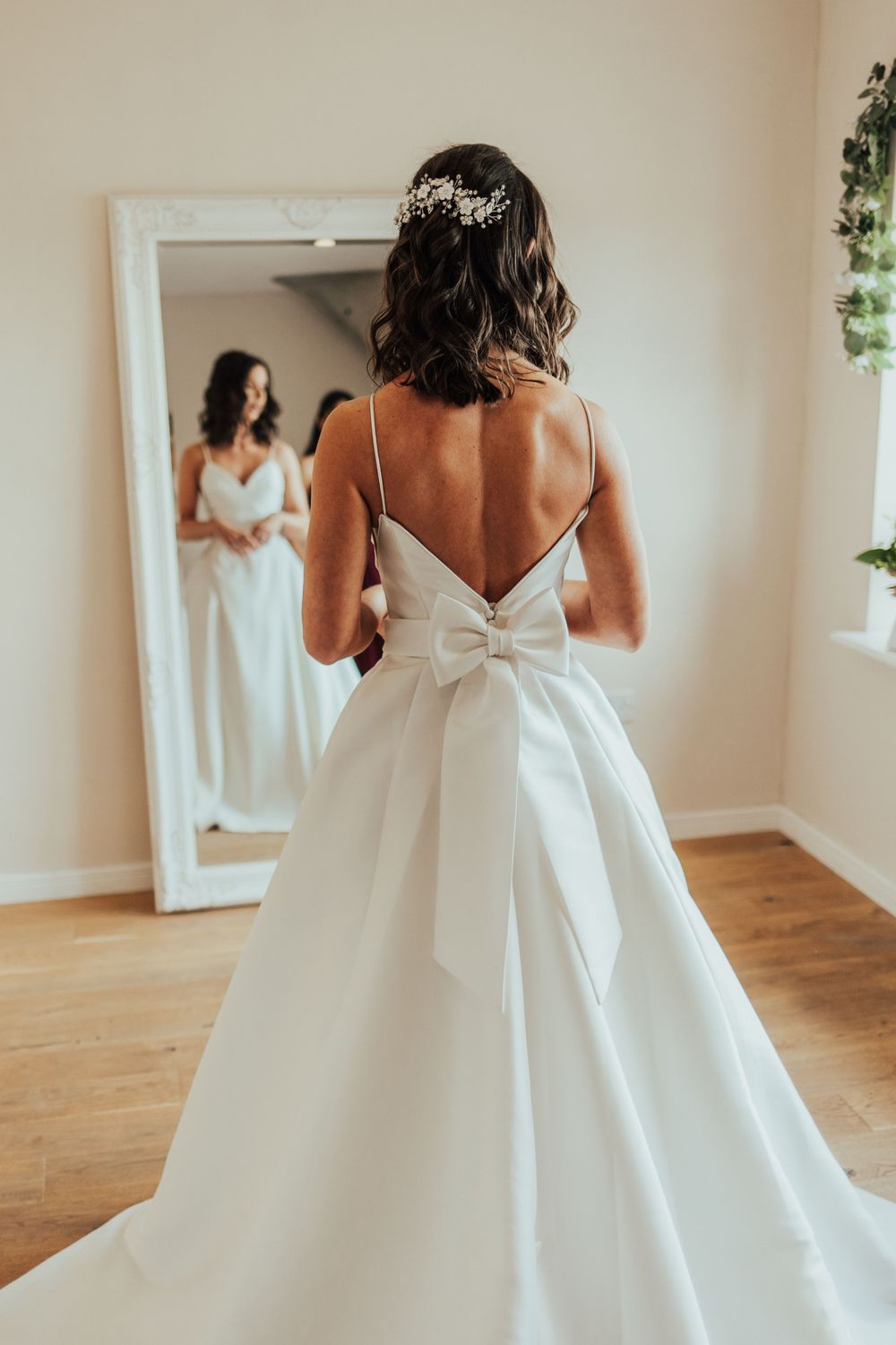 Elegant white wedding dress with open back design shown in natural light setting.