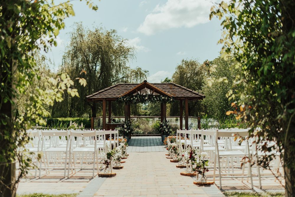 Outdoor wedding ceremony setup with white chairs lined up beneath willow trees.