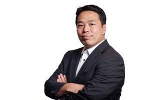 Professional headshot of person in dark business suit with arms crossed against white background.