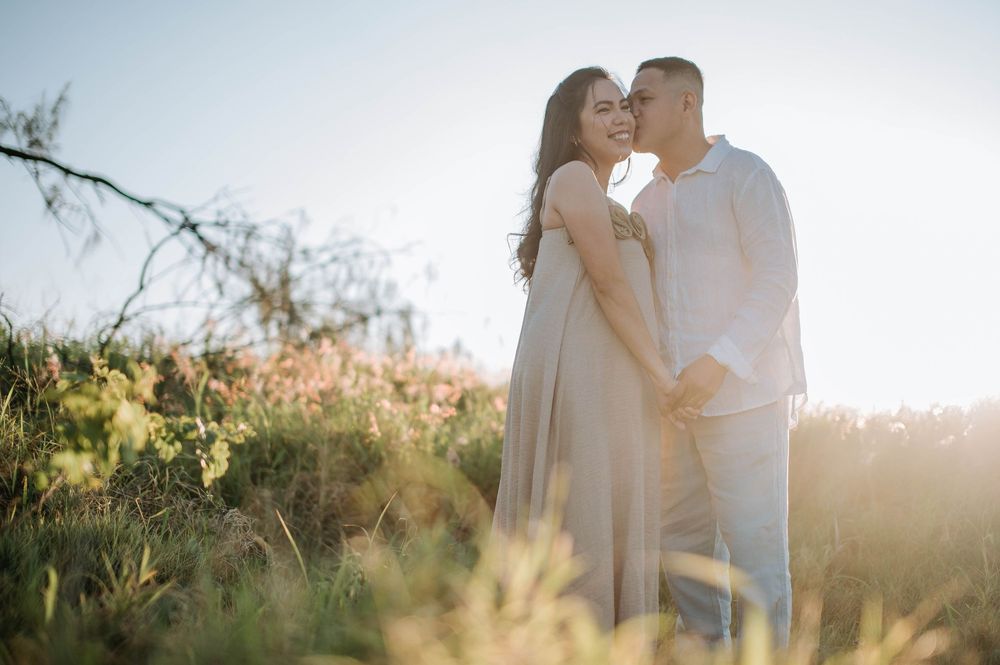 A couple shares a tender moment in a sunlit field of tall grass during golden hour.