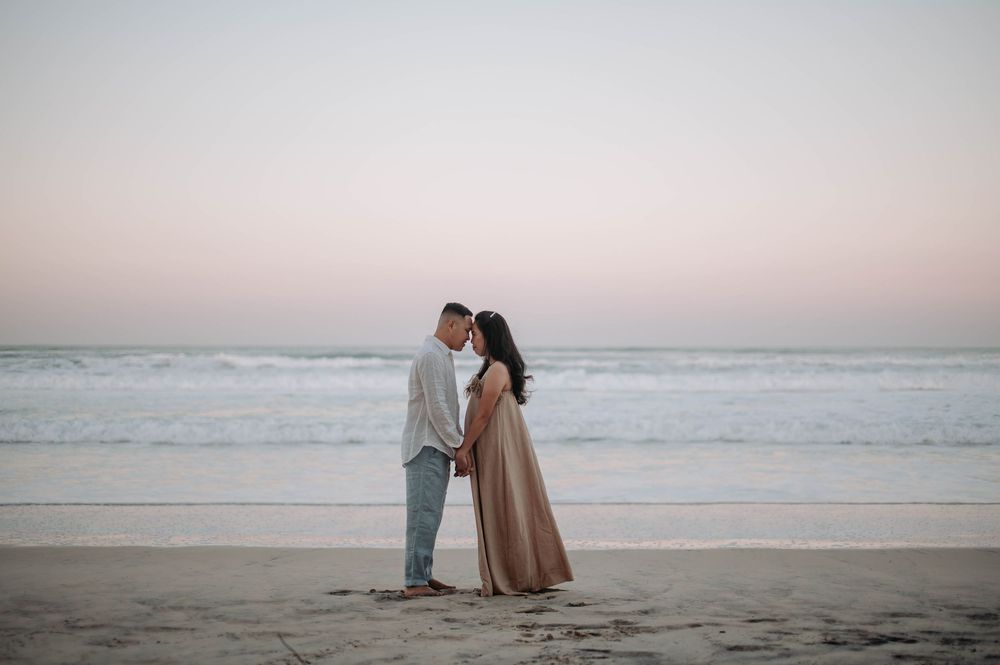 A couple stands silhouetted on a beach at sunset as gentle waves roll onto the shore.