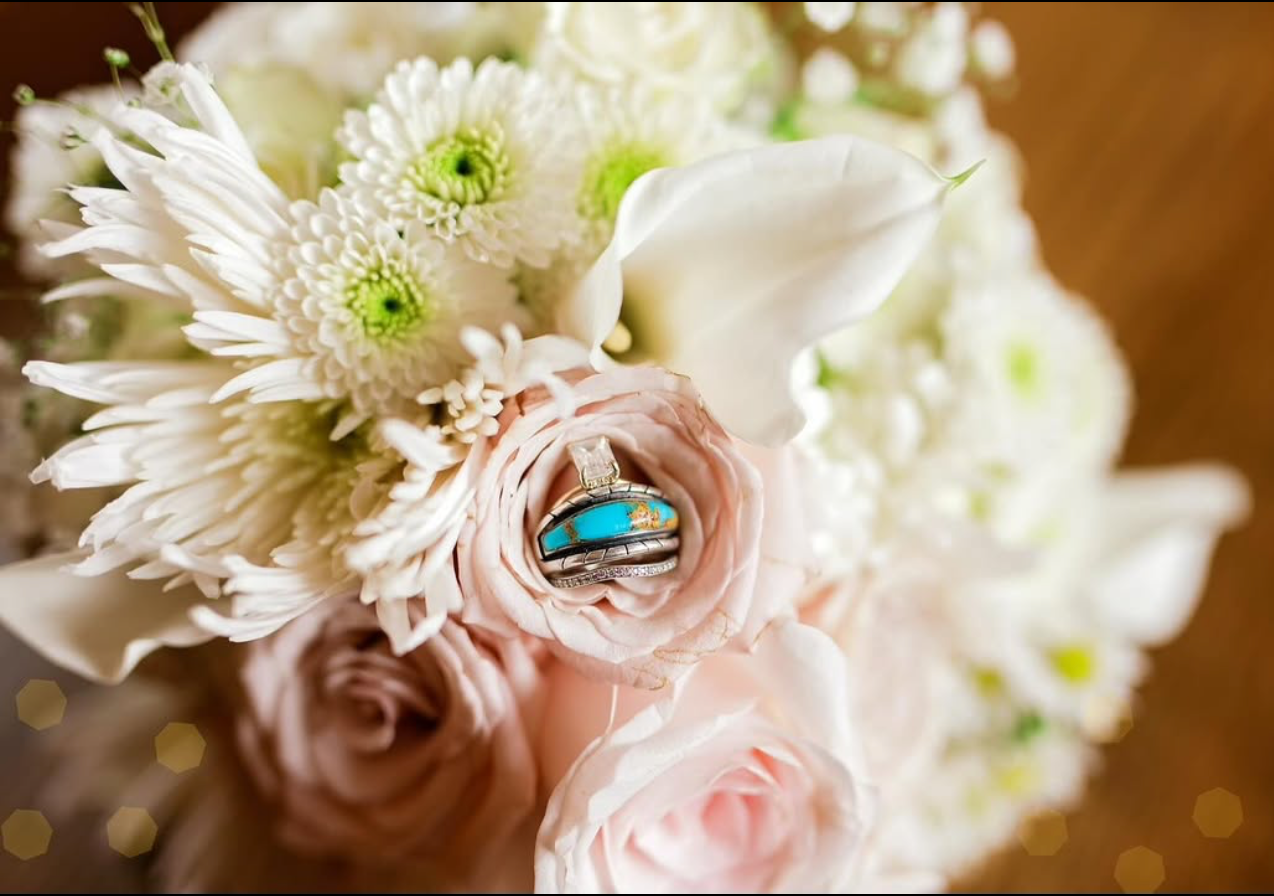 Wedding rings nestled in pink and white flowers with turquoise accents.