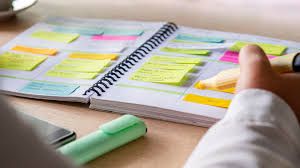 A notebook filled with colorful sticky notes and a mint green highlighter marker on a wooden desk surface.