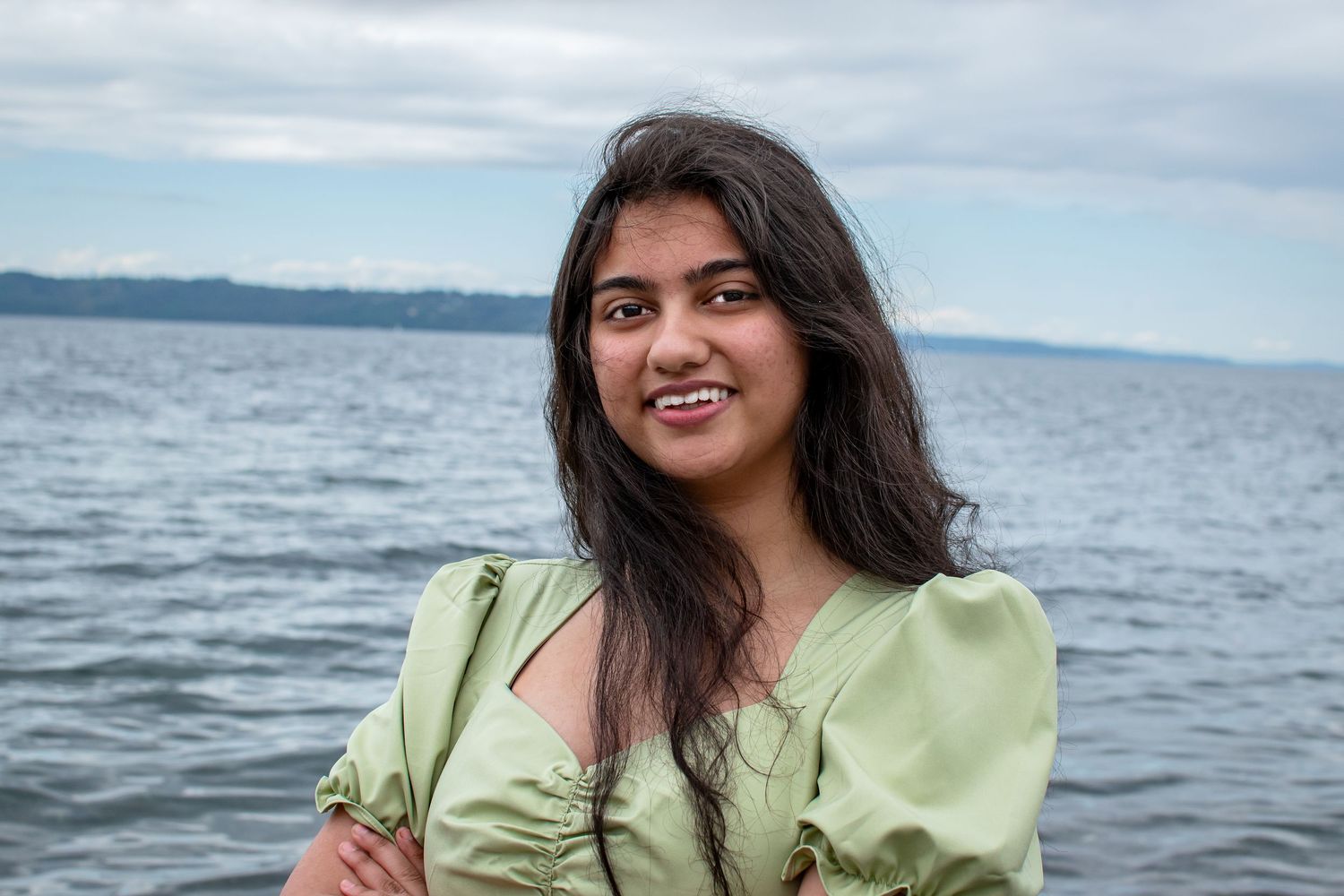 Smiling senior at Redondo Beach in a green dress, captured by the water during a joyful graduation photo session.