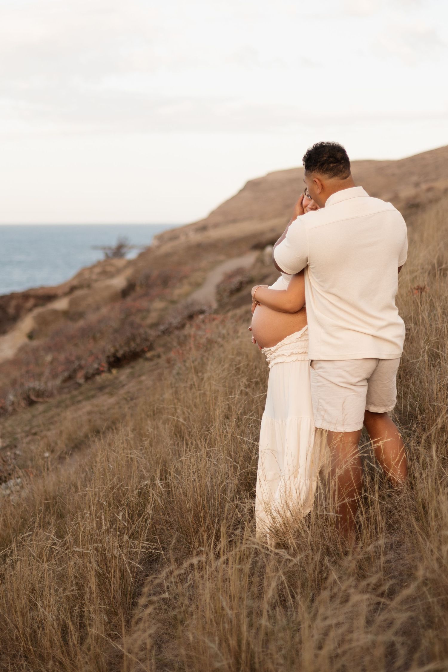 maternity sunset session at taylors mistake, christchurch. Parents cuddling together on the hill, overlooking the beach