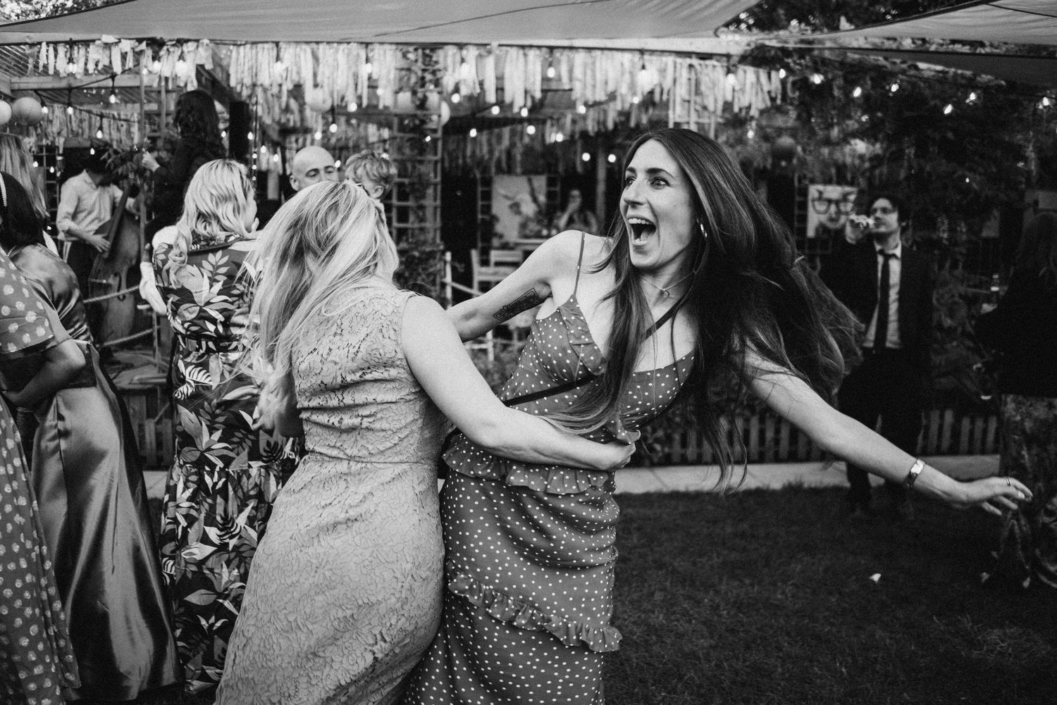 Two carefree women dancing together outdoors at a summer party in black and white photography.
