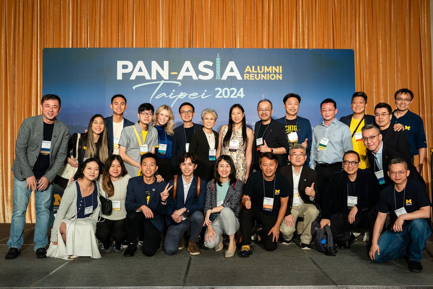 Group photo of alumni gathered at Pan-Asia 2024 event standing together in front of blue branded backdrop.