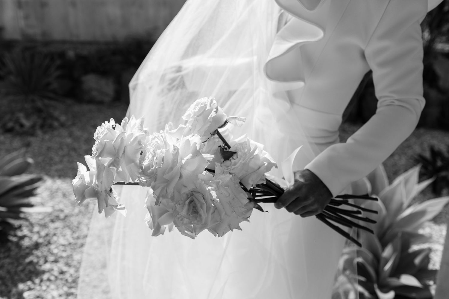 A close-up black and white photo of a bridal bouquet with white flowers against a wedding dress.