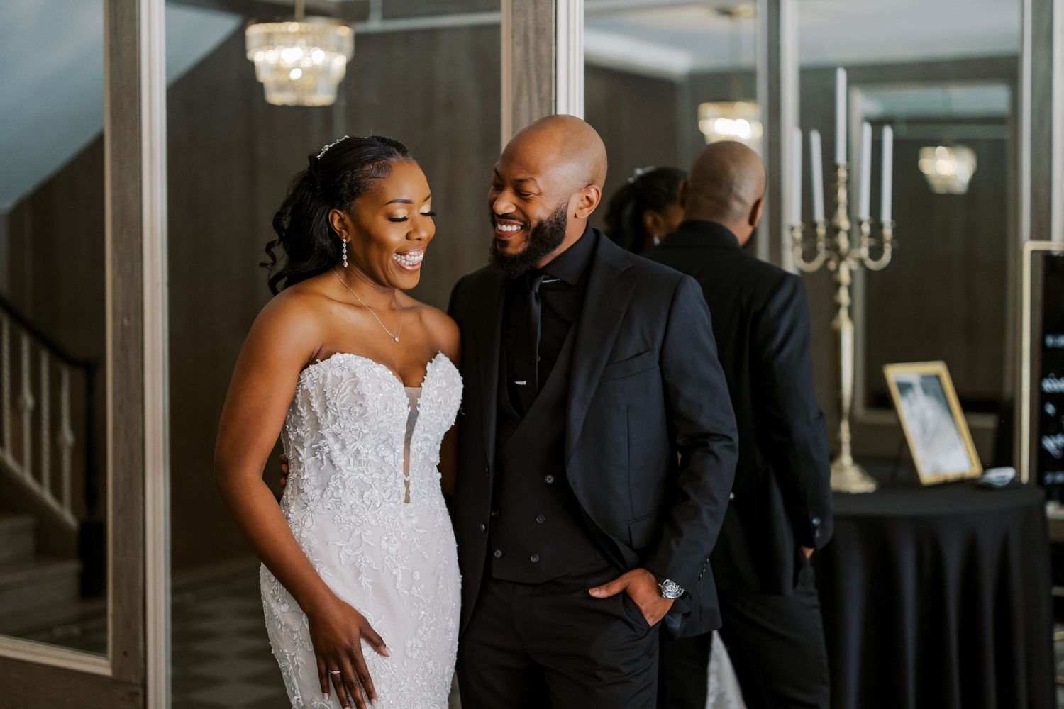 A joyful newlywed couple in formal wedding attire share a candid moment in an elegant indoor venue.
