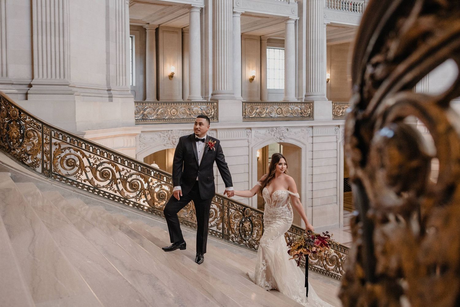 A couple descends an elegant marble staircase with ornate gold railings at the San Francisco City Hall.