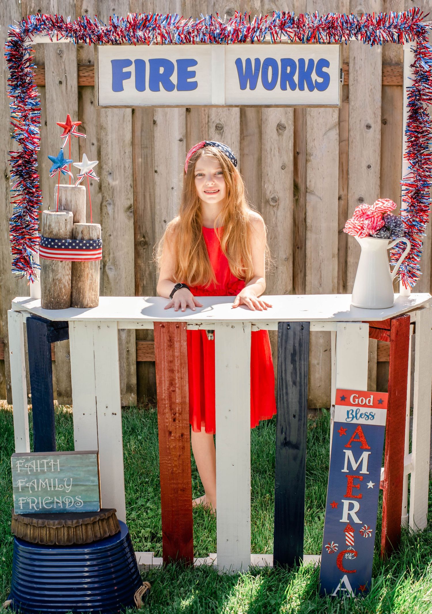 Patriotic fireworks stand display with red white and blue decorations and wooden fence backdrop.