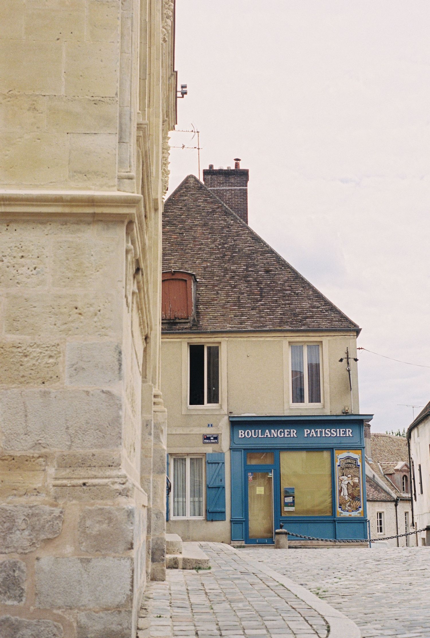 Quaint French bakery with blue storefront on corner of historic stone building.