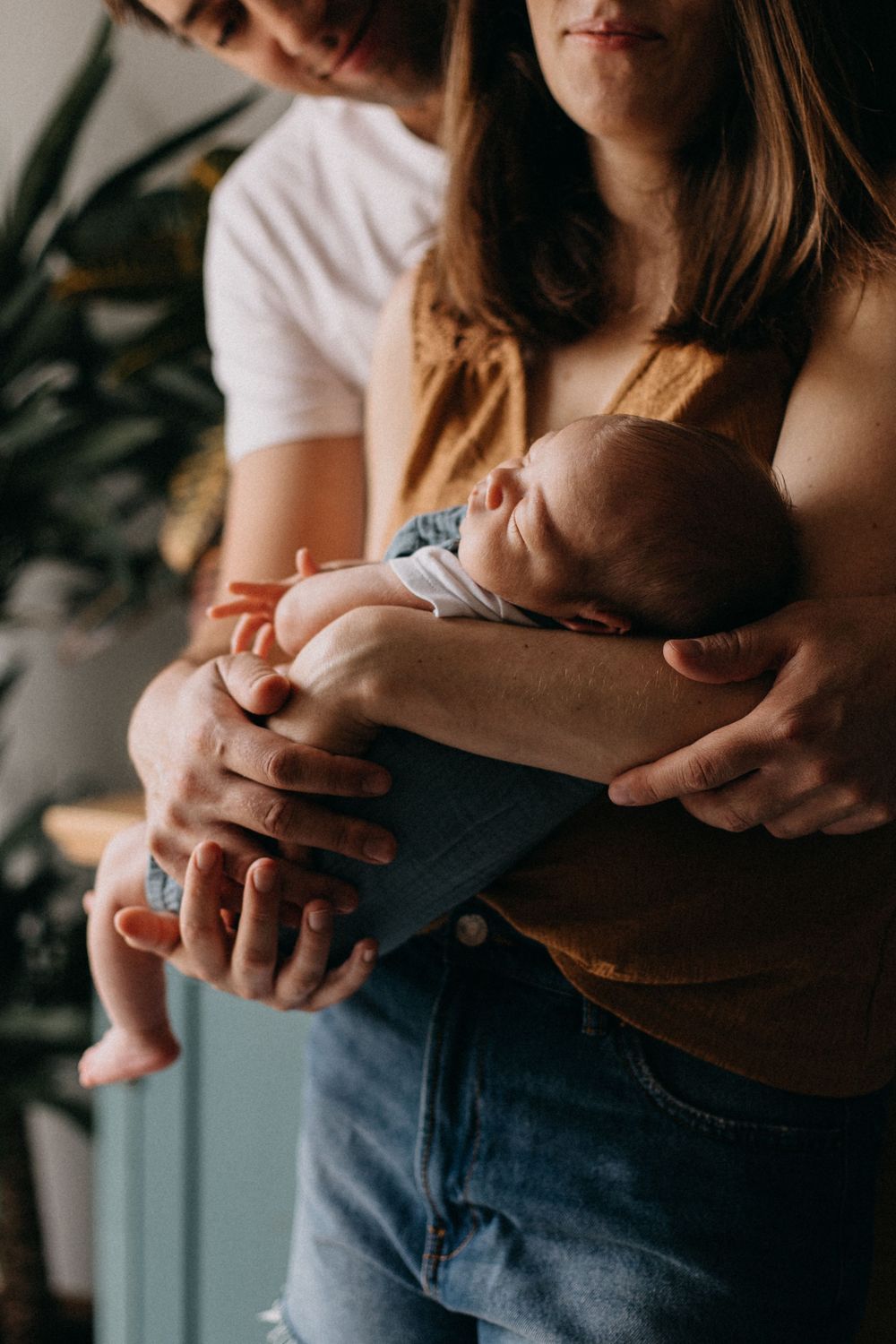 A sleeping newborn baby is gently cradled in loving arms, wearing blue denim overalls.