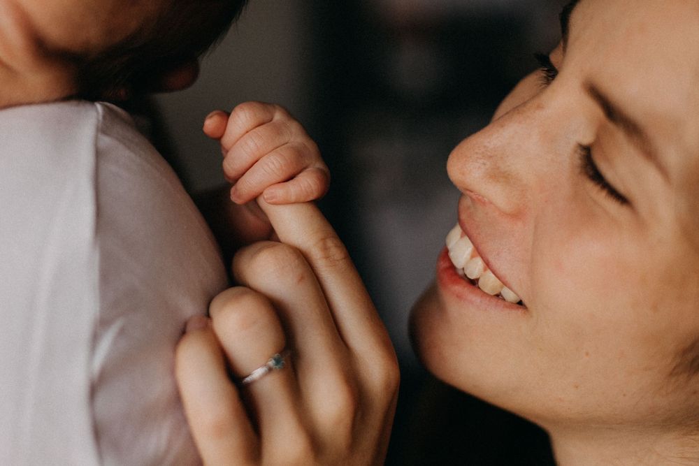 Close up photo showing hands clasped together with a wedding ring visible, with a joyful smile in soft lighting.