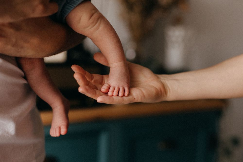 Close-up of gentle hands touching small baby feet in soft indoor lighting.