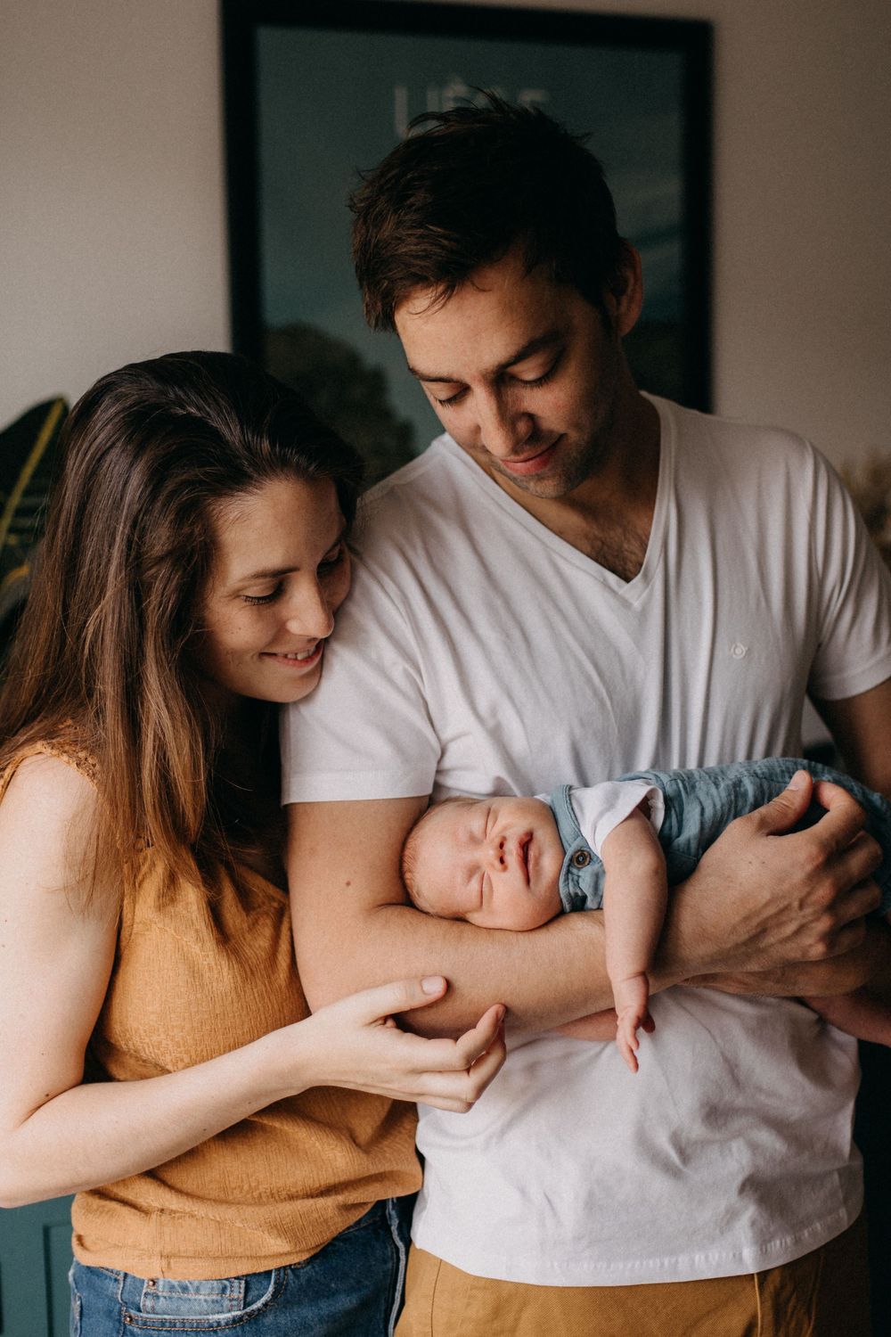 A couple in casual clothing admires their sleeping newborn baby in a tender family moment.