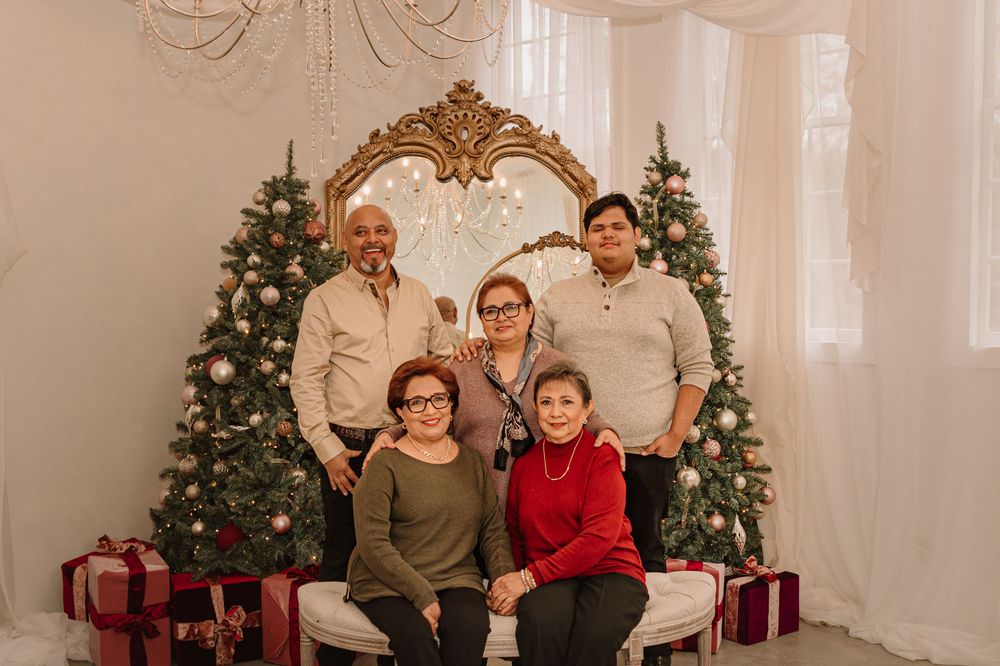 Holiday family portrait with decorated Christmas trees and wrapped presents in background.
