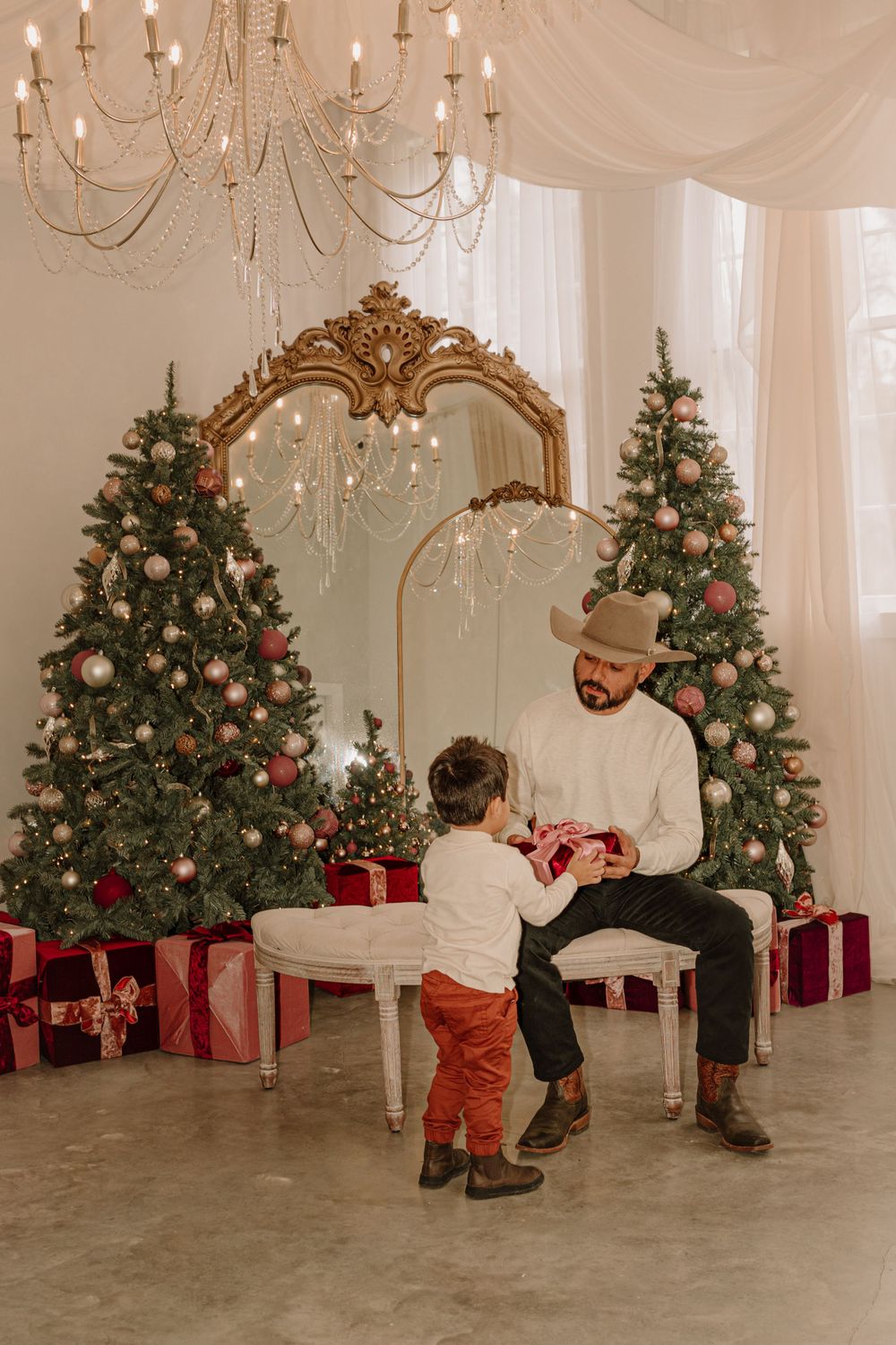 Christmas scene with decorated trees and ornate mirror as parent and child exchange gifts.