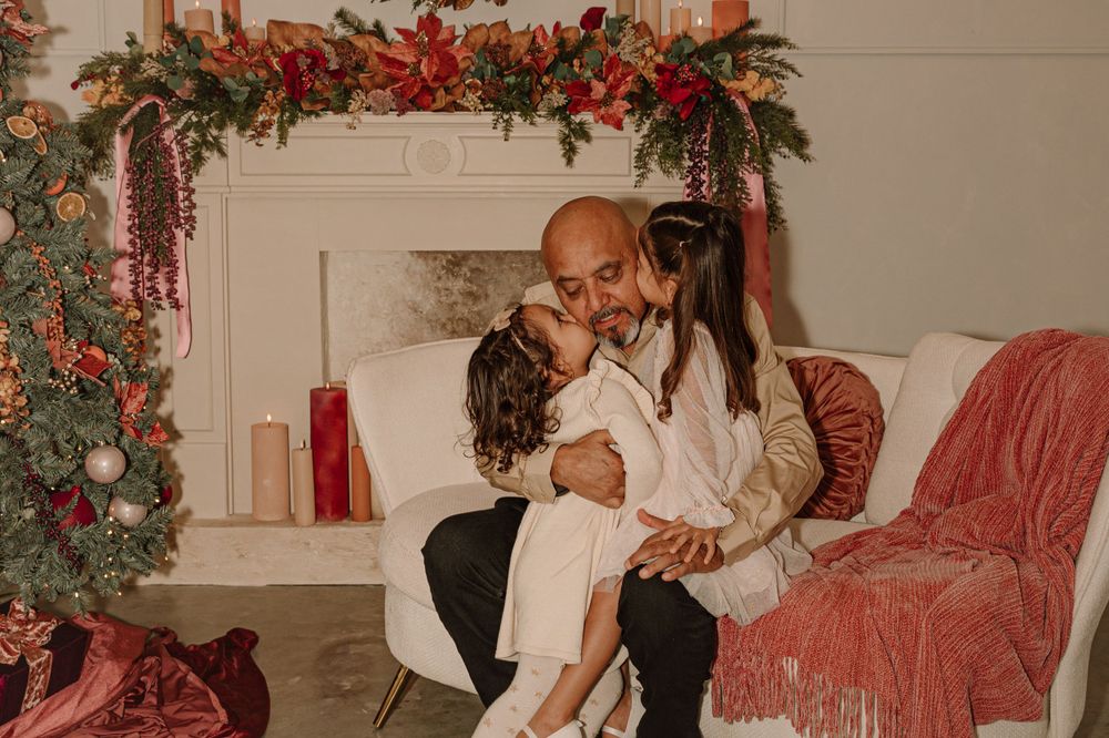 Family moment by Christmas fireplace with holiday decorations and red accents.