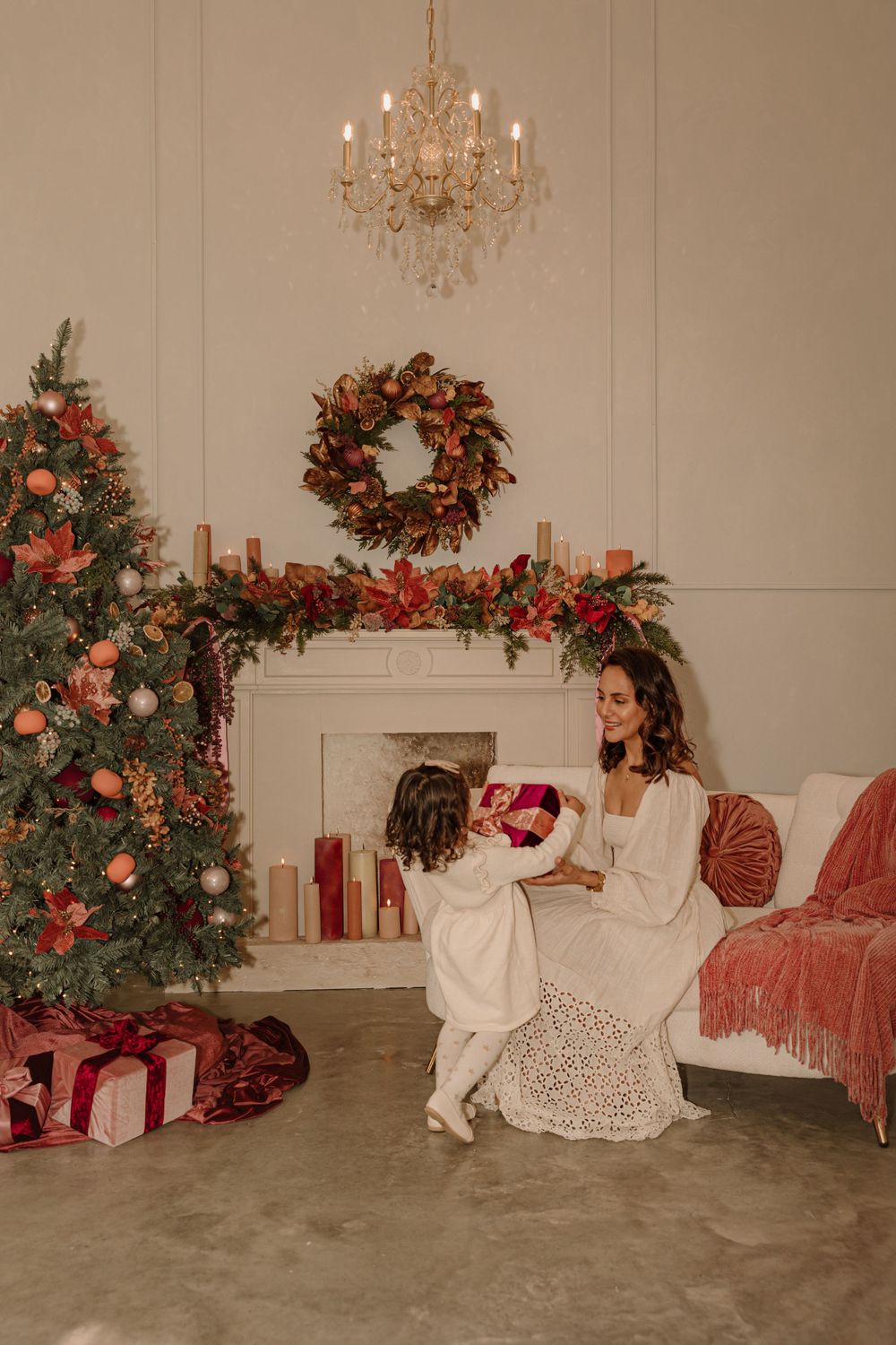 Mother and child sitting by Christmas tree and fireplace exchanging presents.