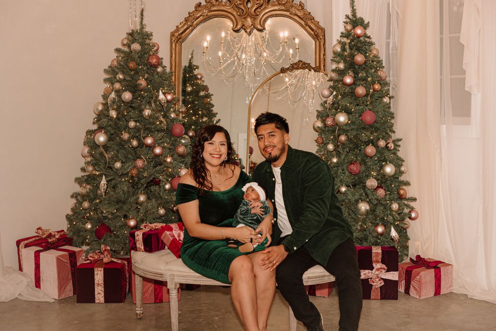 A family poses for a holiday portrait in front of decorated Christmas trees and wrapped presents.