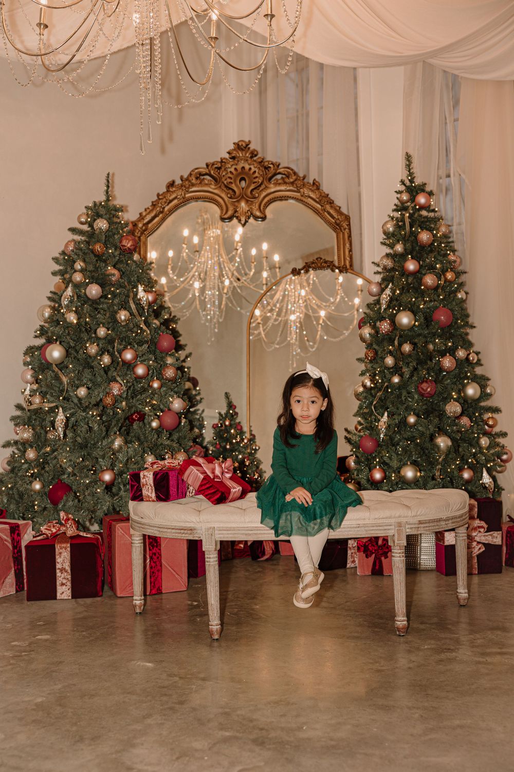 Elegant Christmas setting with twin decorated trees flanking ornate gold mirror and wrapped presents.