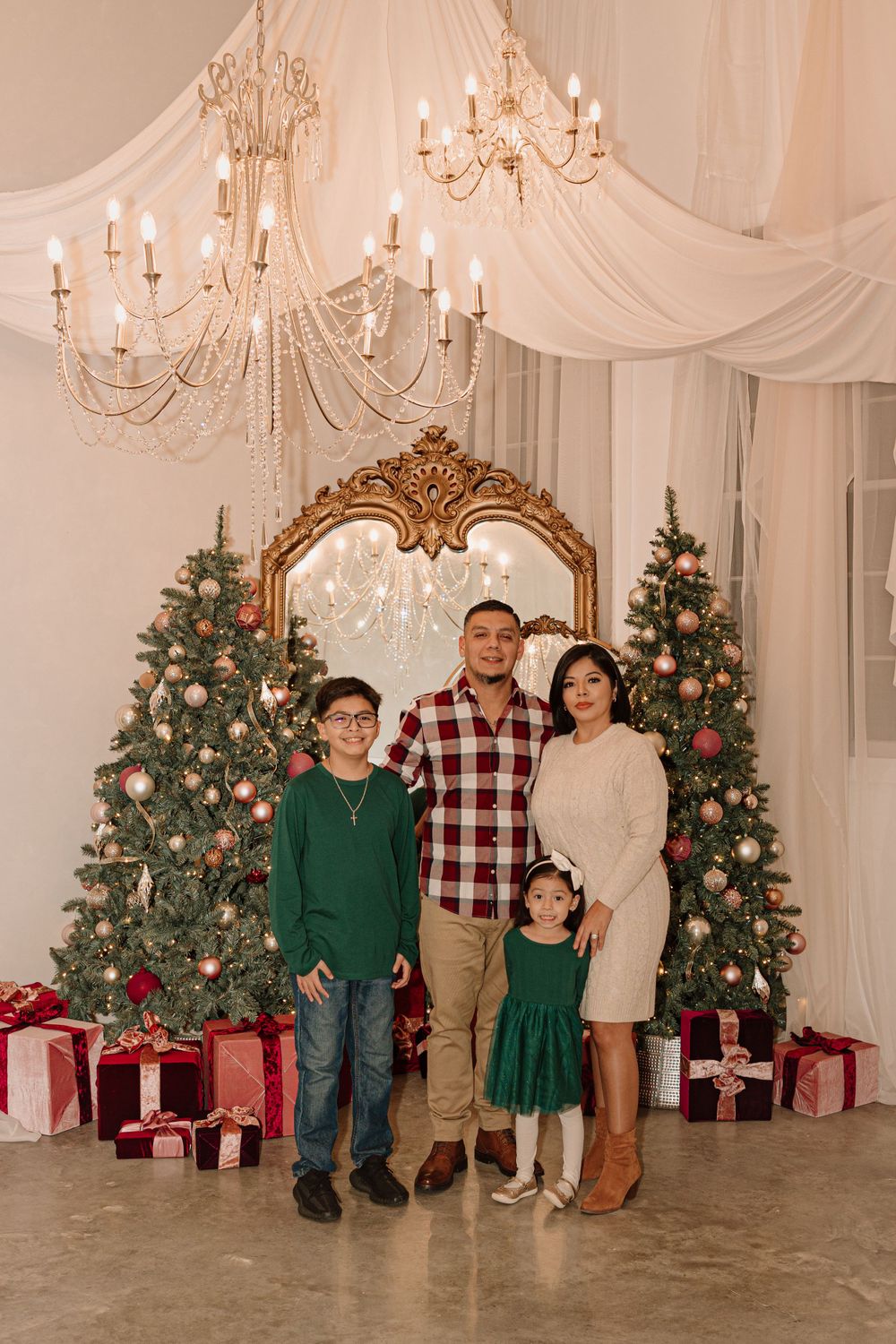 Holiday portrait setup with decorated Christmas trees, gold mirror, white draping and presents.