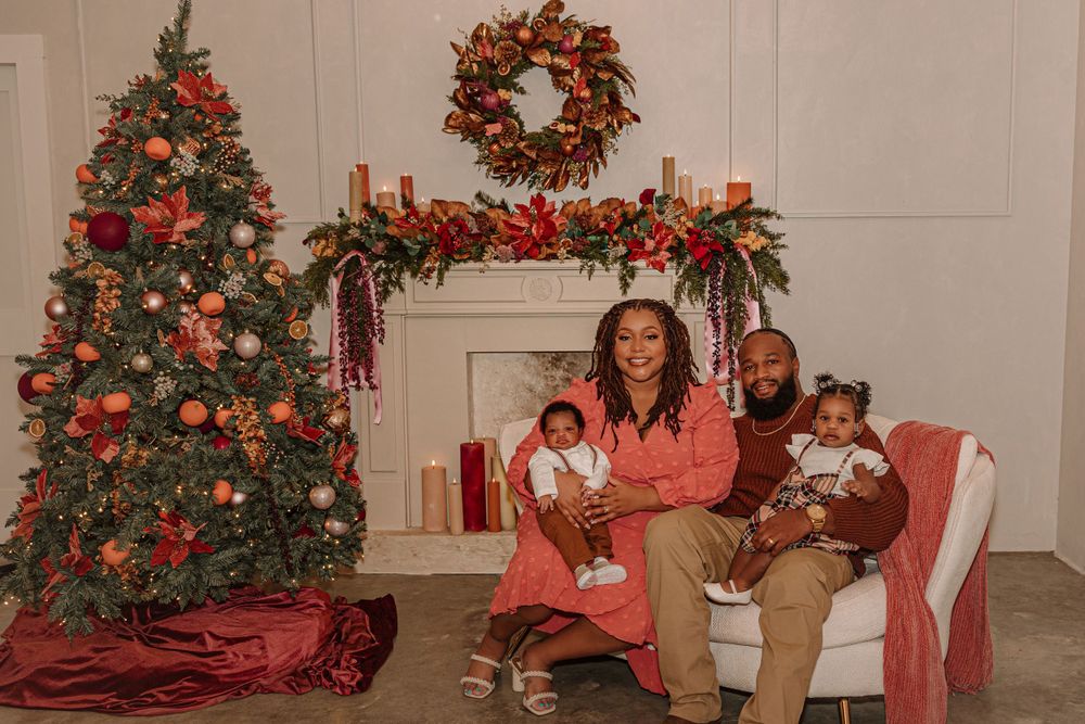 A cozy holiday family portrait in front of a Christmas tree and decorated fireplace mantel.