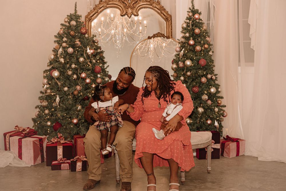 A family group poses for a holiday photo surrounded by Christmas trees and wrapped presents.