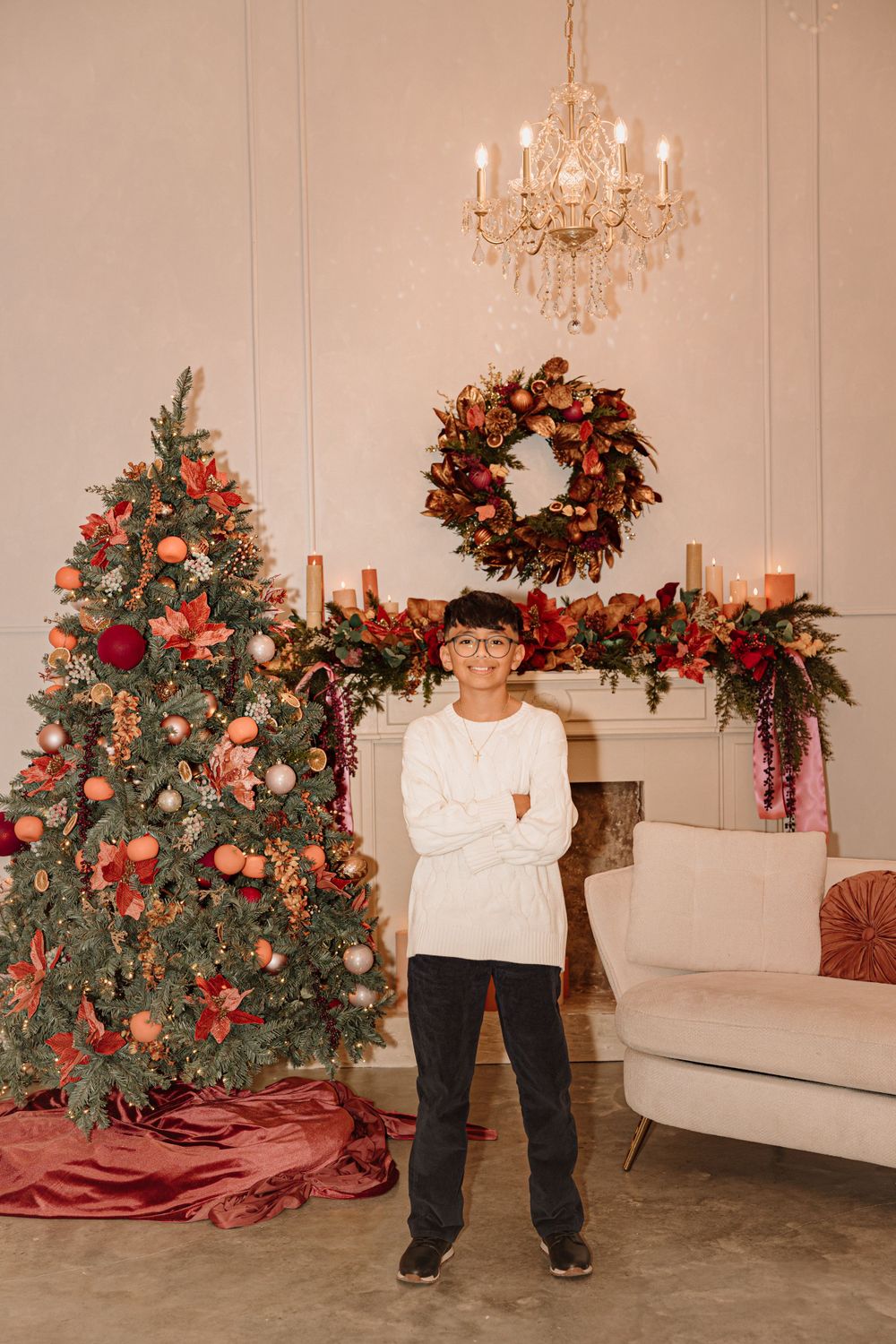 Christmas decorated room with tree, wreath above fireplace, and crystal chandelier.