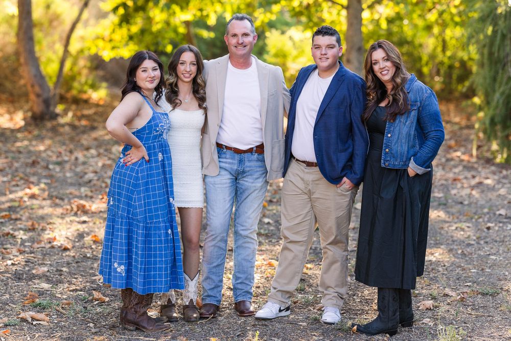Group portrait outdoors on autumn path with casual and dressy attire against background of golden leaves.