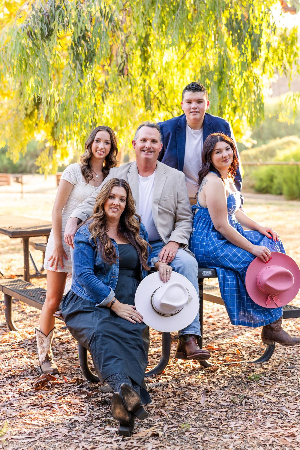 Group posed together outdoors under hanging willow tree branches on a sunny autumn day wearing casual western attire.