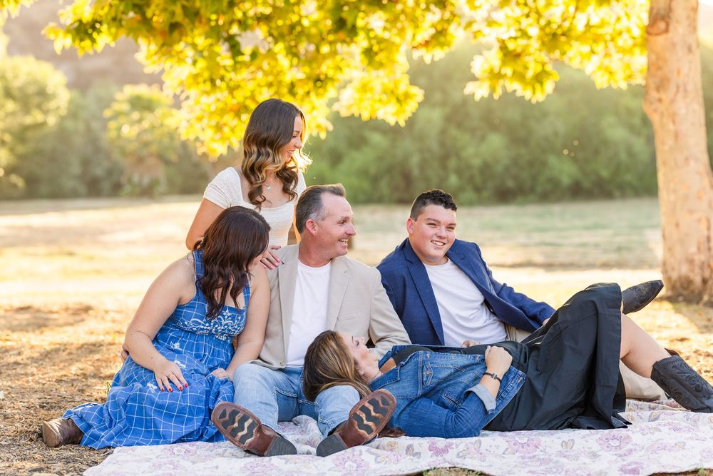 Family group relaxing together on a picnic blanket under golden autumn trees in warm evening sunlight.