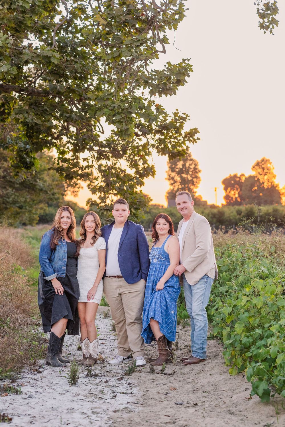A group stands together on a dirt path at sunset with trees and greenery in the background.