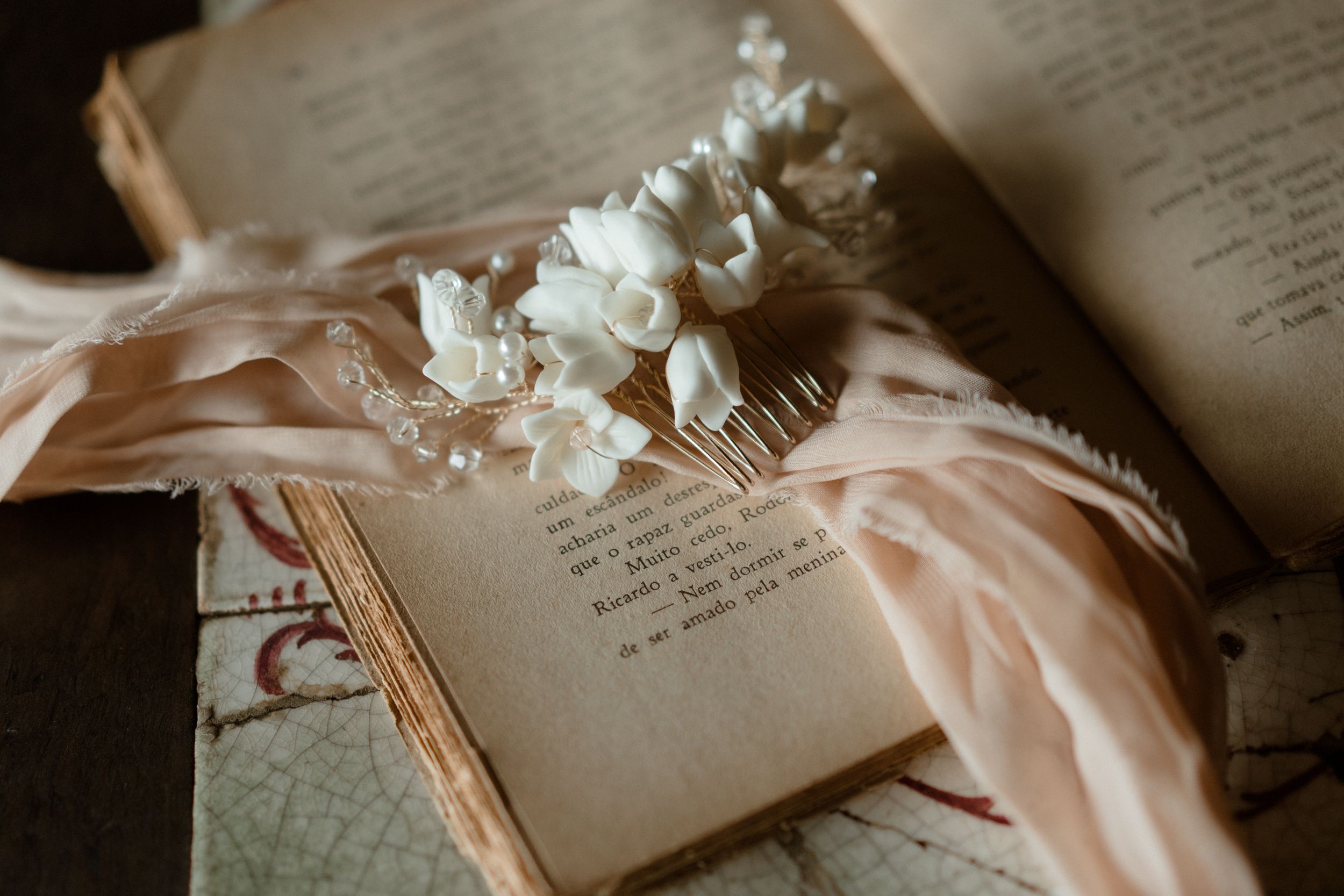 Delicate white flowers resting on open book pages with soft peach fabric.