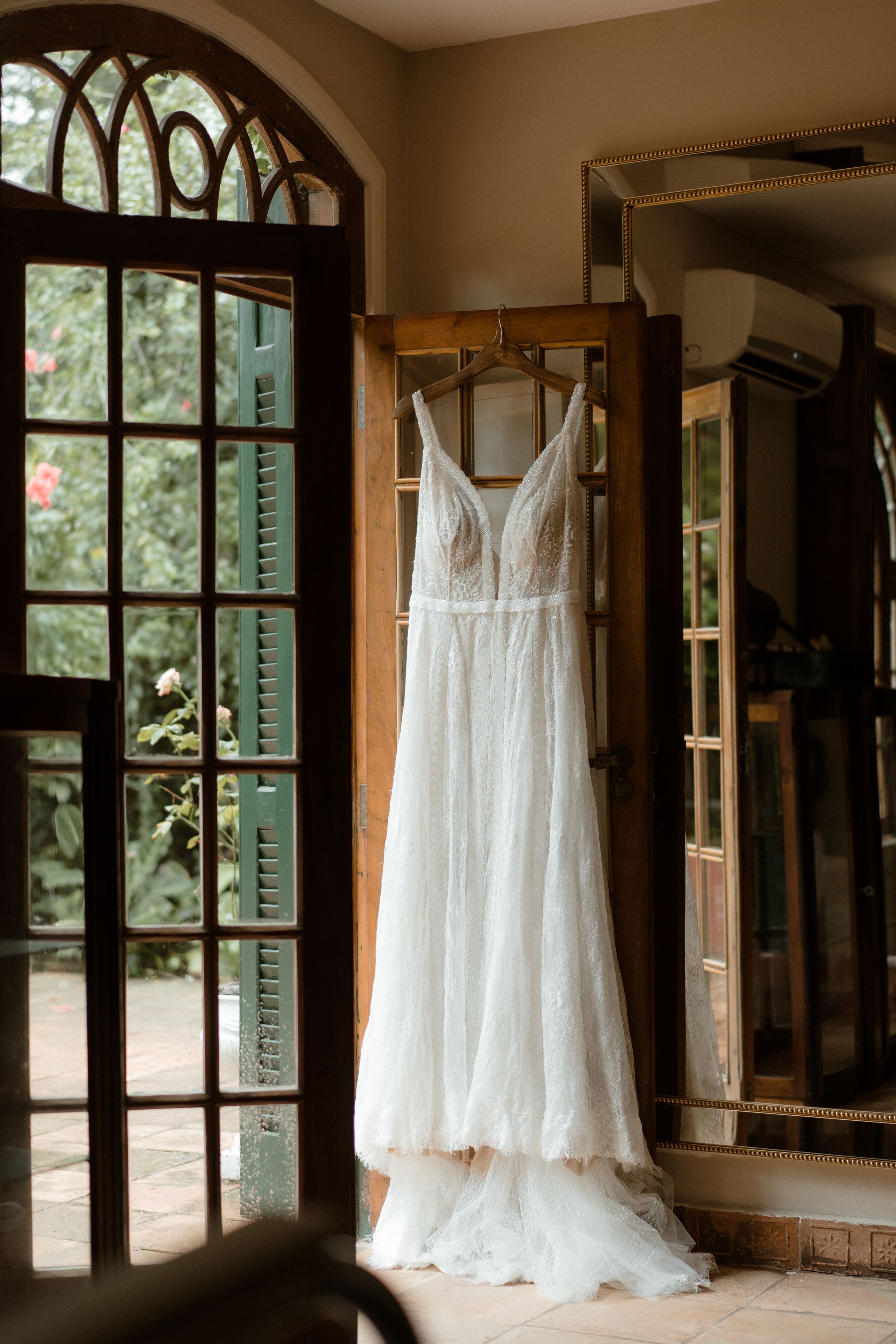 White wedding dress hanging in doorway with arched window and natural lighting.