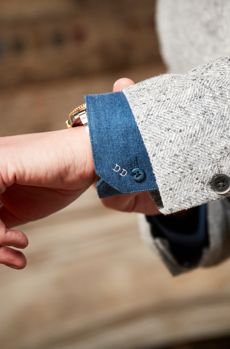 Close-up view of a blue shirt with personalised initials and grey herringbone jacket fabric.