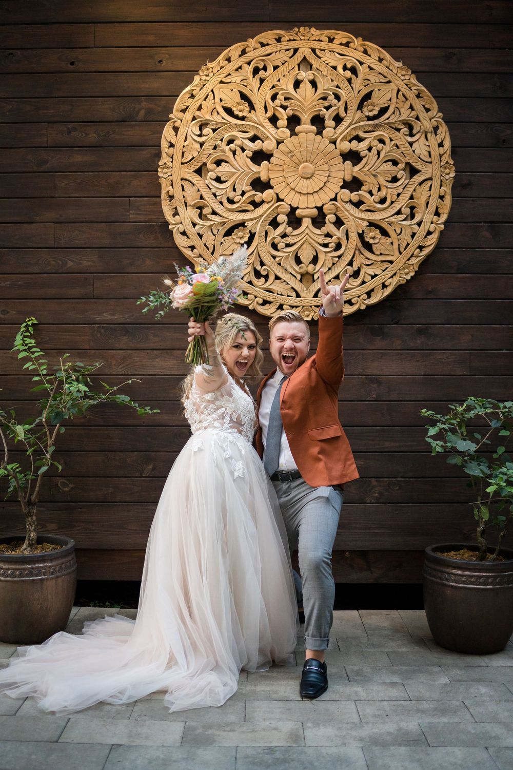 Wedding couple celebrates joyfully beneath an ornate circular wooden wall medallion.