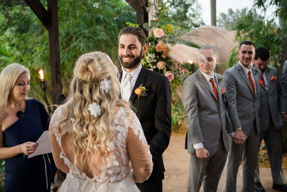 A candid wedding moment outdoors with guests and bridal party standing beneath trees with autumn decor.