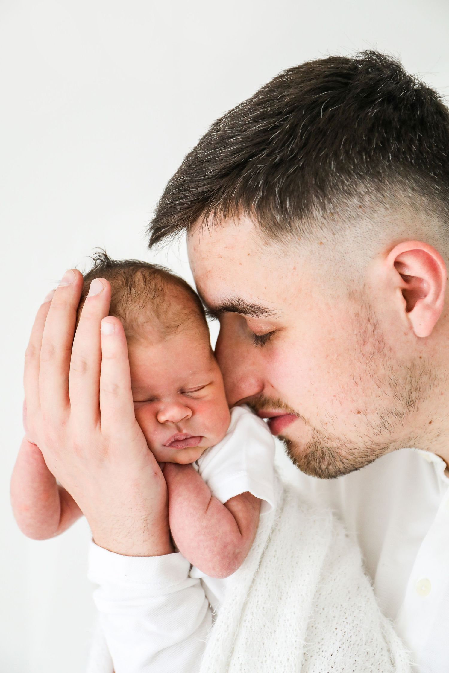 A parent tenderly cradles a sleeping newborn baby against their face in a heartwarming portrait, during newborn shoot in Nottingham