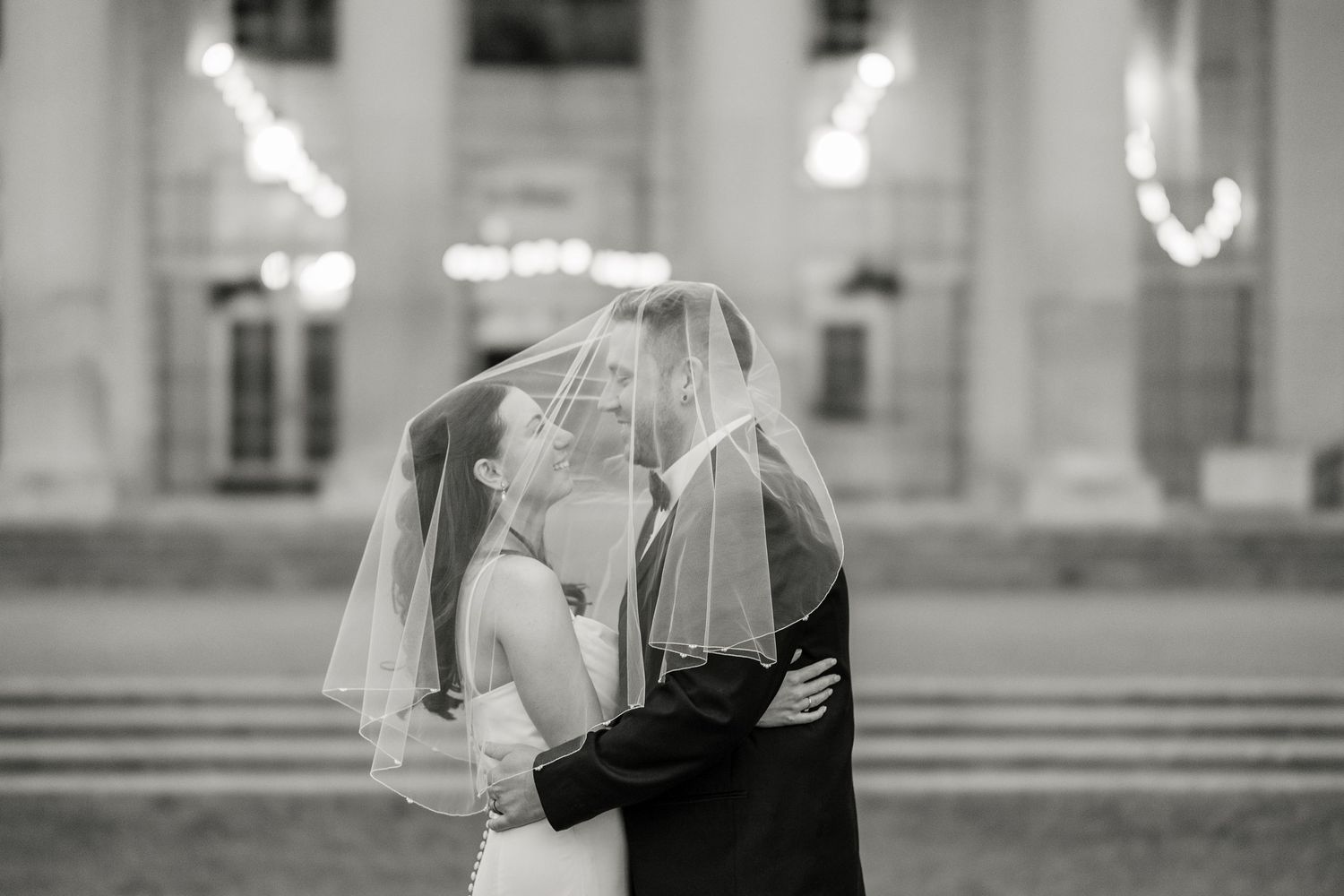 A romantic black and white photograph of a couple embracing under a wedding veil at their ceremony at Hall of Springs.