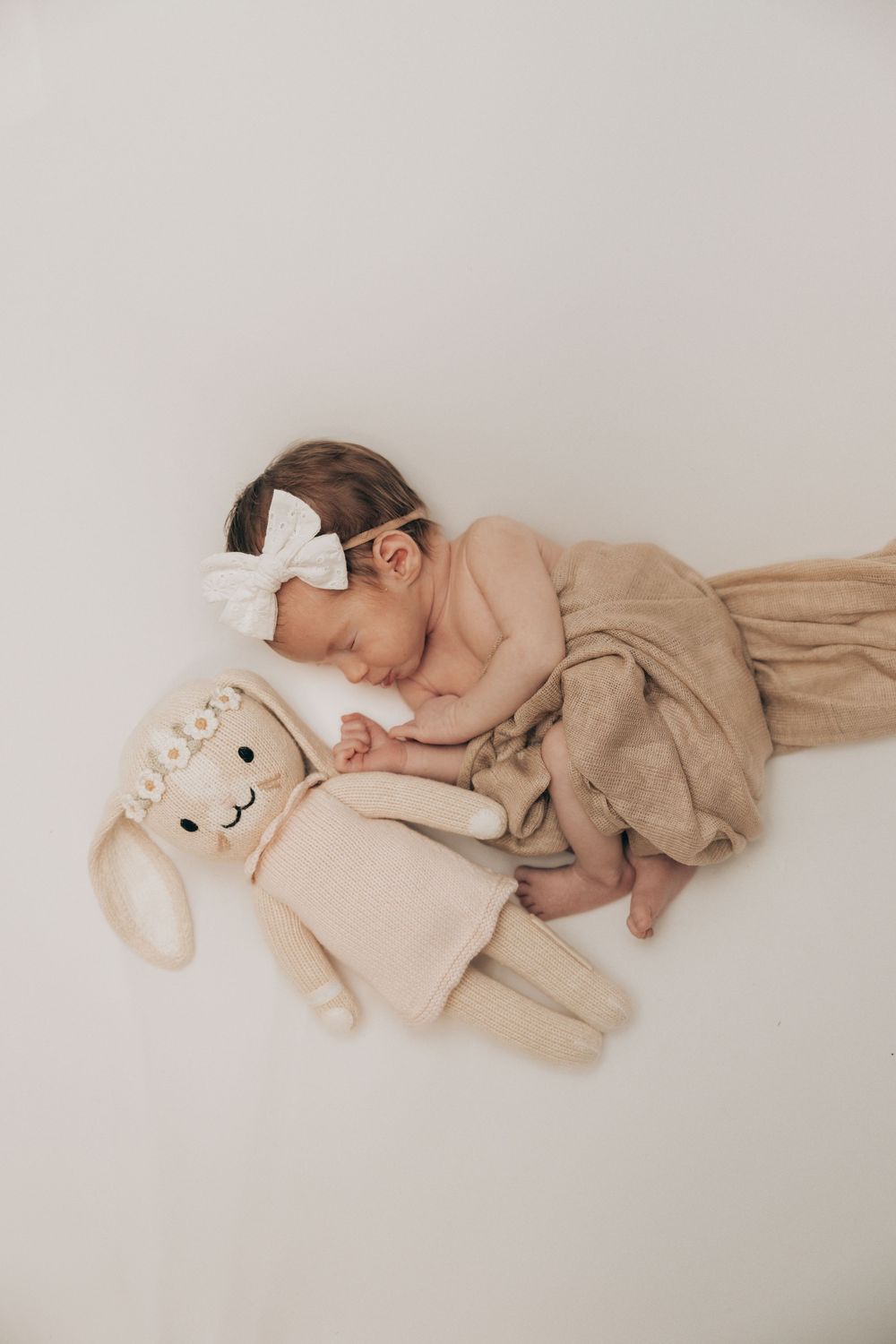 Sleeping baby in neutral tones cuddling with plush bunny toy on white background.
