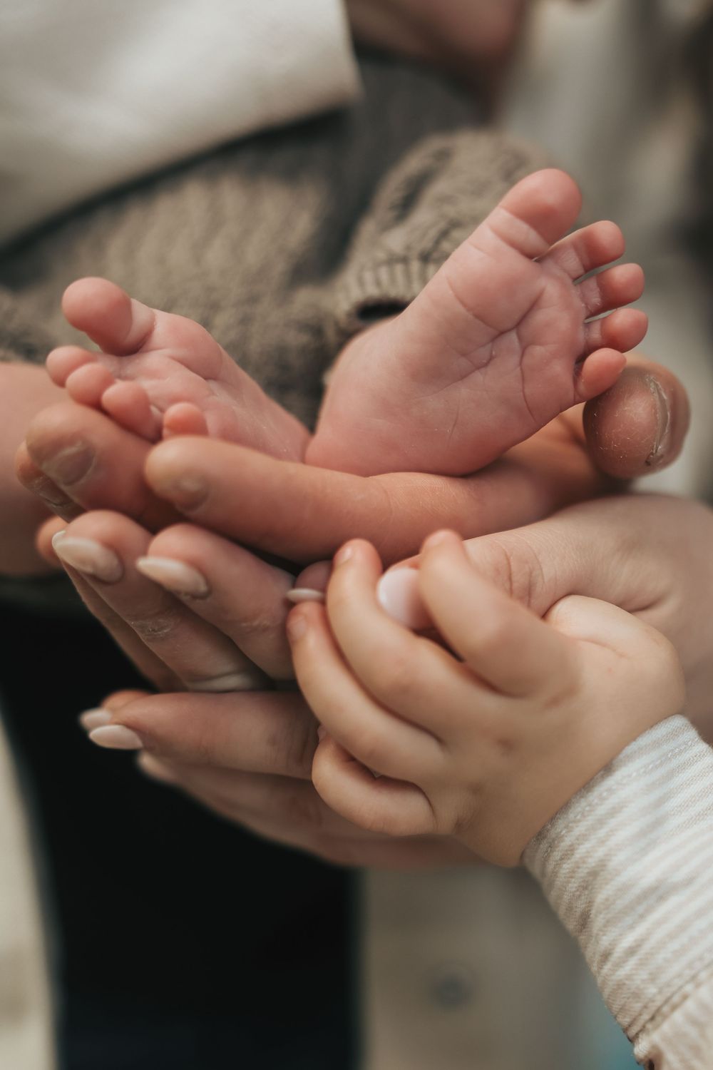 Close-up of tiny newborn baby feet cradled gently in adult and child hands, symbolizing family love.