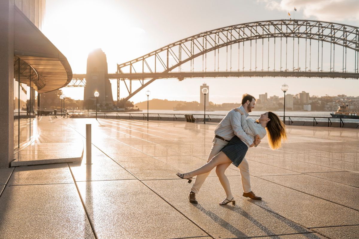 couple is dancing in front of the harbour bridge with a golden setting sun in Sydney during a photoshoot